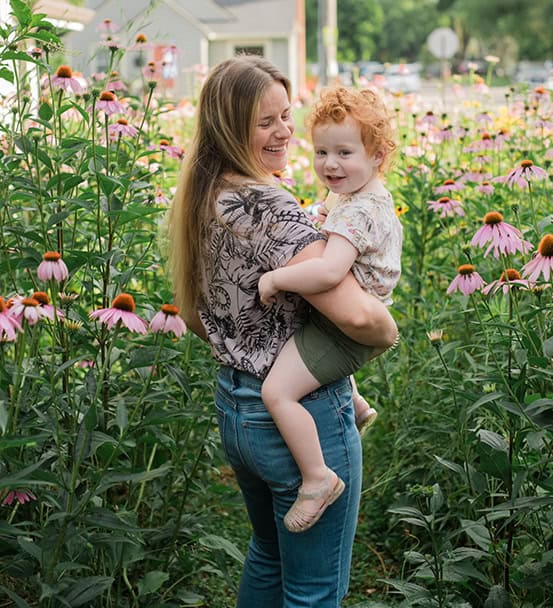 Hannah Monroe holding her daughter in her native plant garden in Indianapolis, surrounded by echinacea